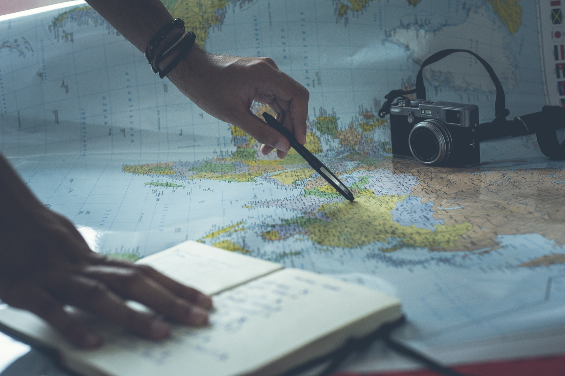 Mężczyzna wskazuje długopisem na państwo na mapie świata. Zapisuje w notatniku rady dla kreatywności